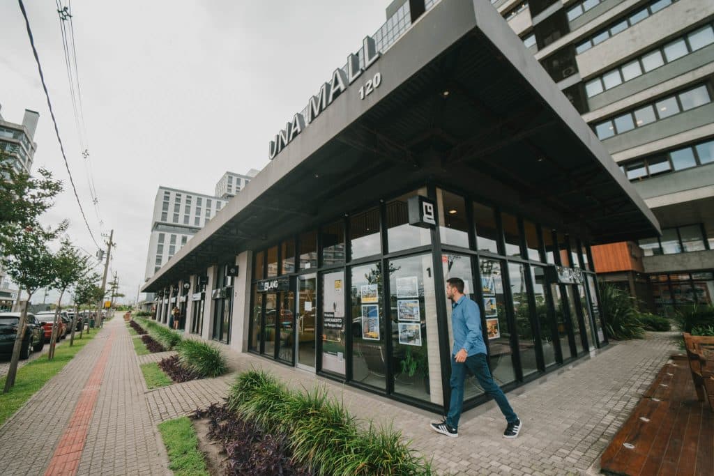 Imagem do UNA Mall, um hub corporativo moderno, com fachadas de vidro e a presença de pedestres na área externa, localizado no Parque Una Pelotas